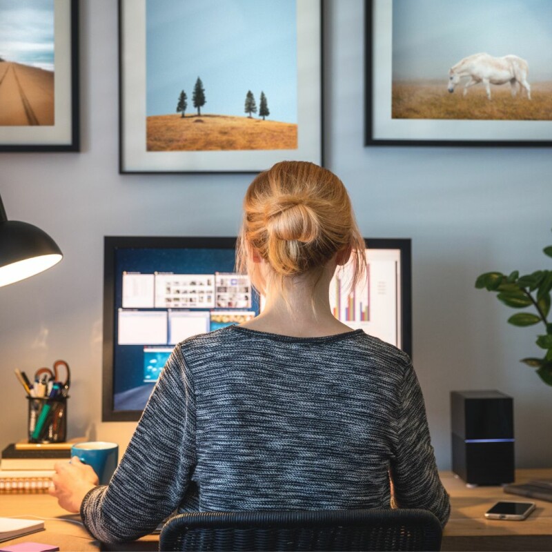 A woman sits at her desk in her home office, on her computer.