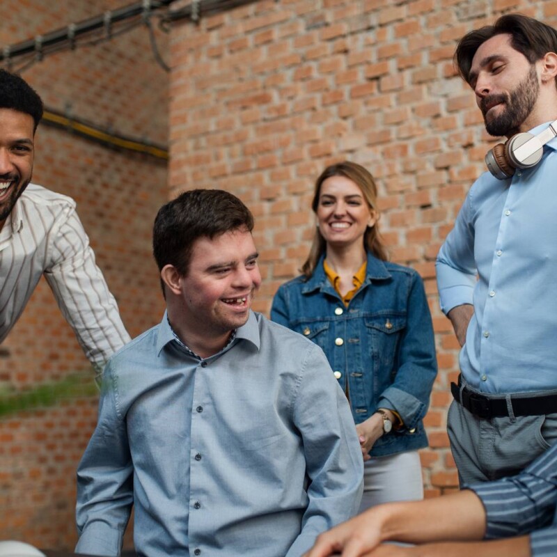 A group of employees who come from different backgrounds sit around together and smile, demonstrating workplace diversity and inclusion.
