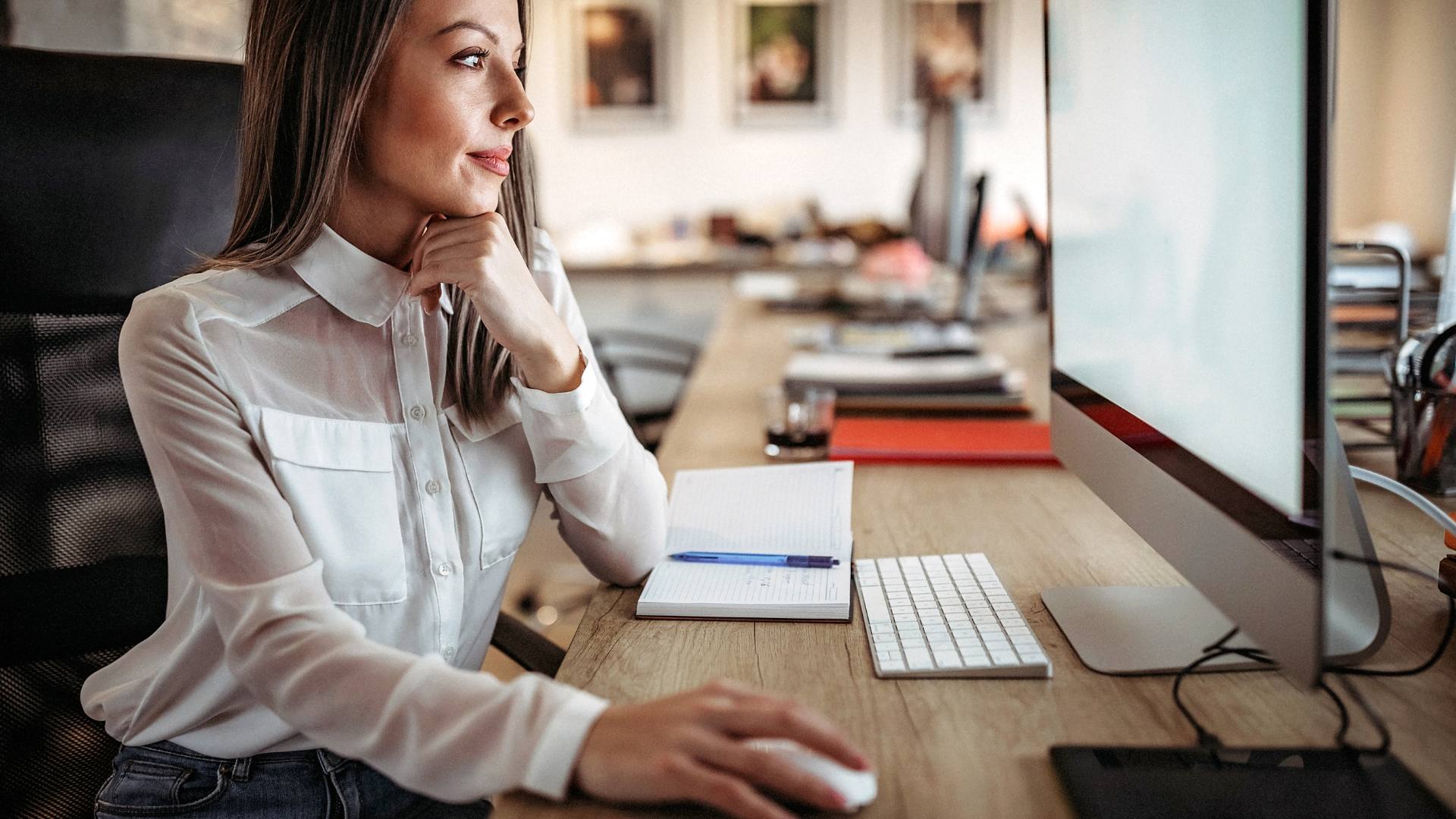 An administrative professional sitting at her computer, using a Canva infographic to enhance her job performance.