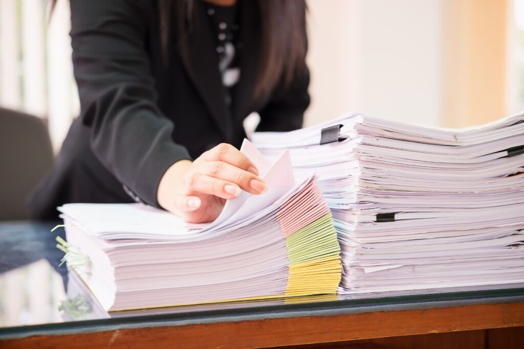 Legal secretary managing multiple complex legal documents at a desk.