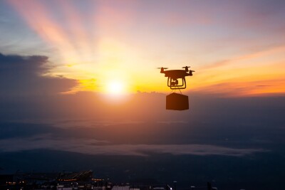 Delivery drone carrying package flying in front of a sunset
