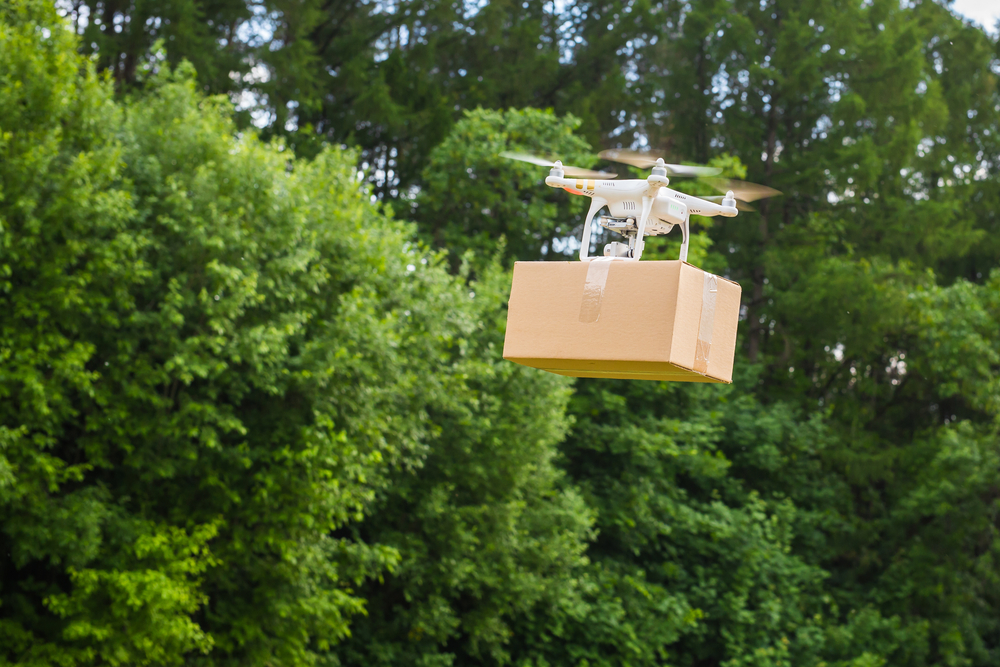 Drone flying in the air carrying a cardboard box for delivery
