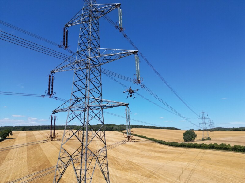 Drone flying near electric transmission tower.