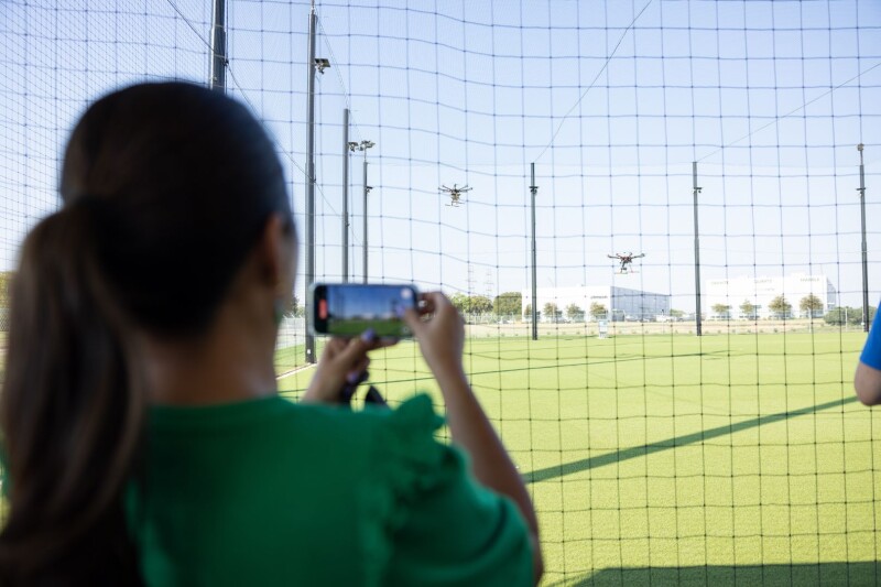 Woman holding phone recording drones flying in netted research area