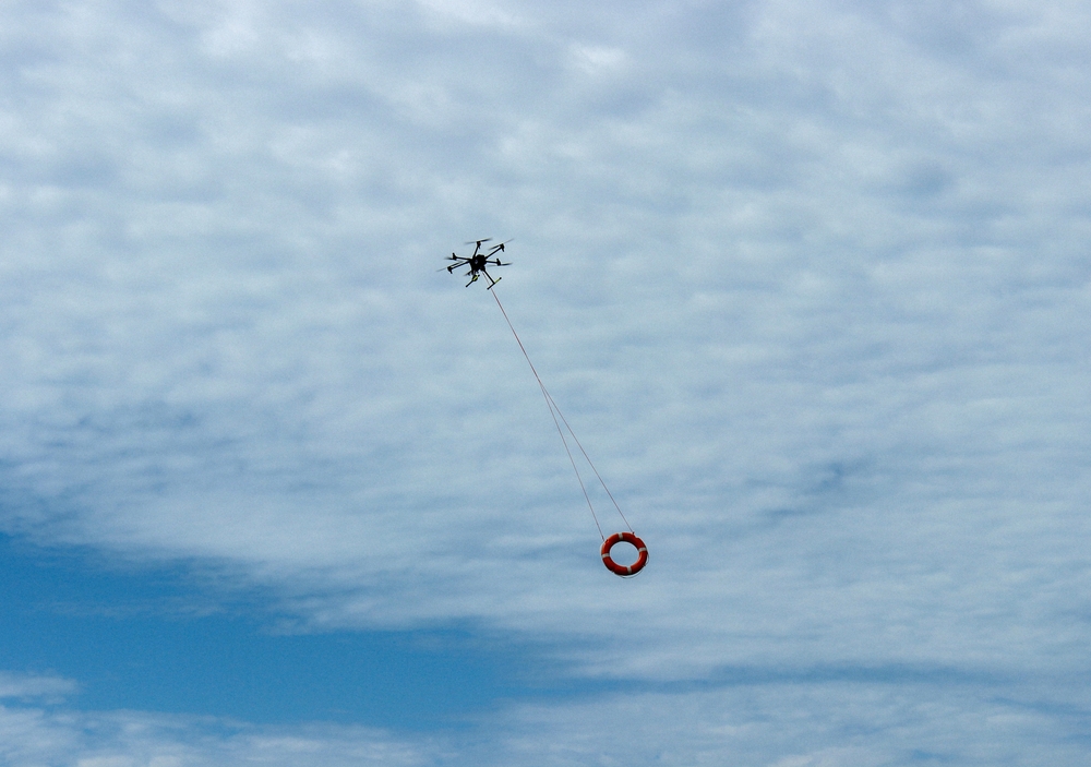 Powerful rescue drone in action over the beach, flying to save lives by lifting a lifebuoy to assist drowning individuals in the sea.