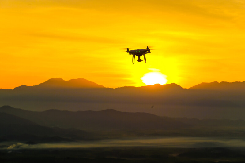 drone flying near a mountain range away from the sunset