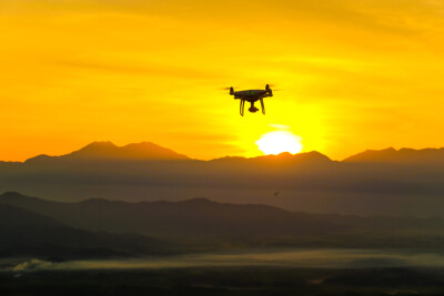 drone flying near a mountain range away from the sunset