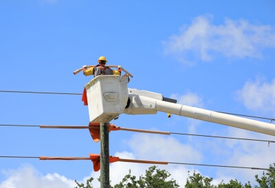 Electrical contractor in a bucket truck insulates live power lines on old wooden poles.