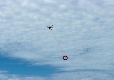 Powerful rescue drone in action over the beach, flying to save lives by lifting a lifebuoy to assist drowning individuals in the sea.