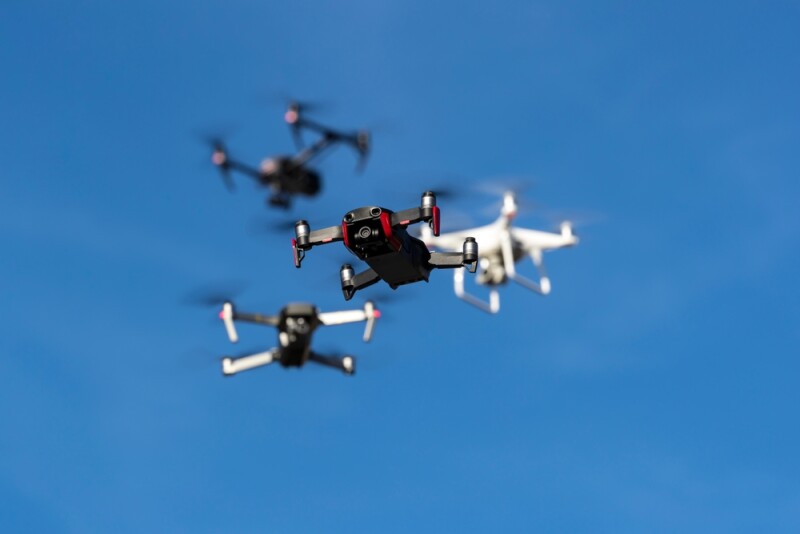 A diverse fleet of drones of all sizes and weights soars through a clear blue sky, their sleek frames glinting in sunlight as they maneuver gracefully in synchronized flight.