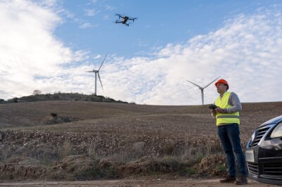 Technician using a remote control for drone inspection of wind turbines in a rural landscape, symbolizing energy innovation and maintenance