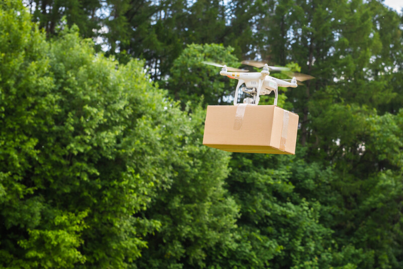 Drone flying in the air carrying a cardboard box for delivery