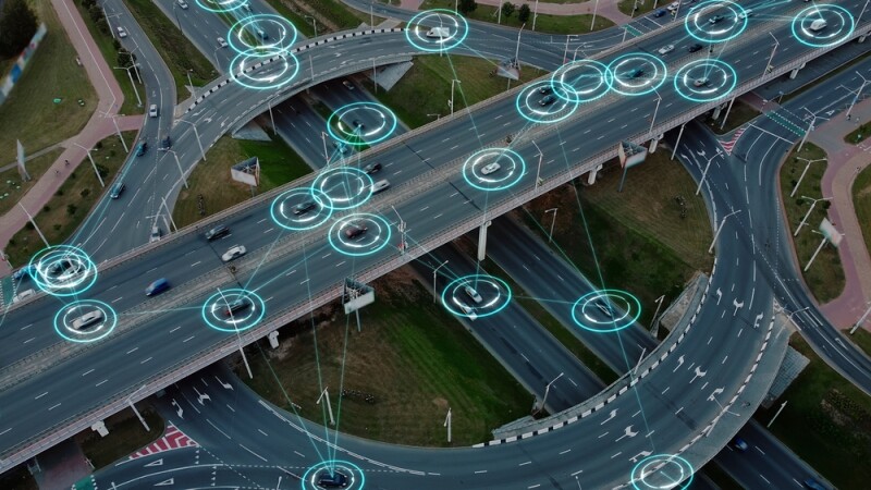 Aerial view: Self-driving autonomous electric cars of the future with HUD elements move along a busy traffic intersection.