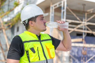 Construction worker in a hard hat and safety vest drinking water, staying hydrated during work on a building site.