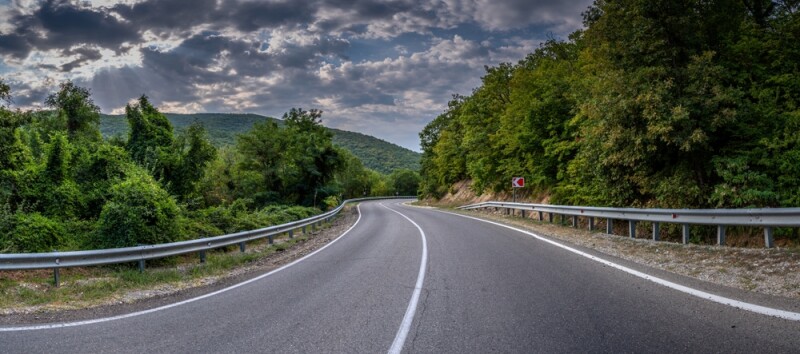 Empty long mountain road to the horizon on a sunny summer day with dramatic cloudy sky.