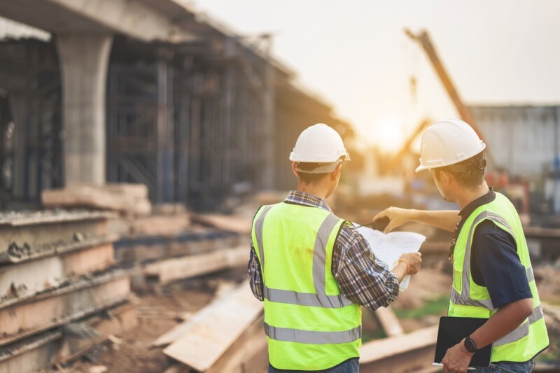 A team of civil engineers and architects wearing safety gear inspect the construction site of a high concrete bridge at a highway construction site.