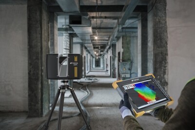 Laser scanner on a tripod in an empty hallway with person holding tablet showing scan data.