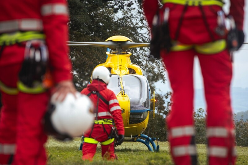 Rear view of team of emergency medical service. Doctor and paramedics with safety harness and climbing equipment running to helicopter.
