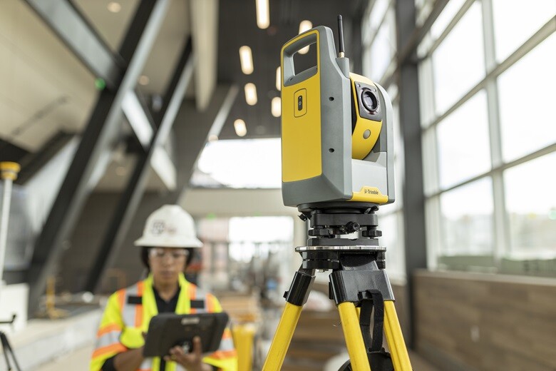 Trimble laser scanner in the foreground with worker holding tablet in the background.