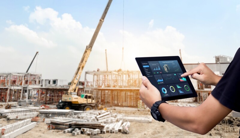 Hands using digital tablet with Construction Management Software on blurred construction site as background