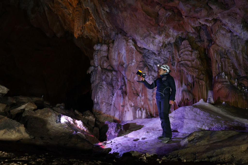 A person stands in an open area of a cave with a handheld SLAM scanning device.