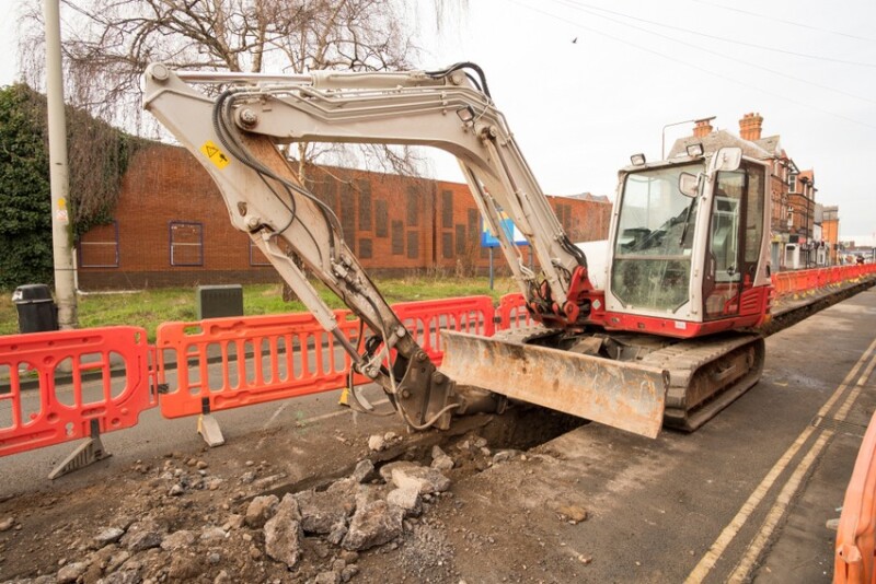 Excavator digging a trench alongside a road.