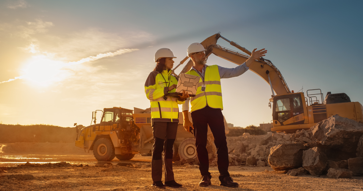 Two professionals at a construction site looking at a computer.