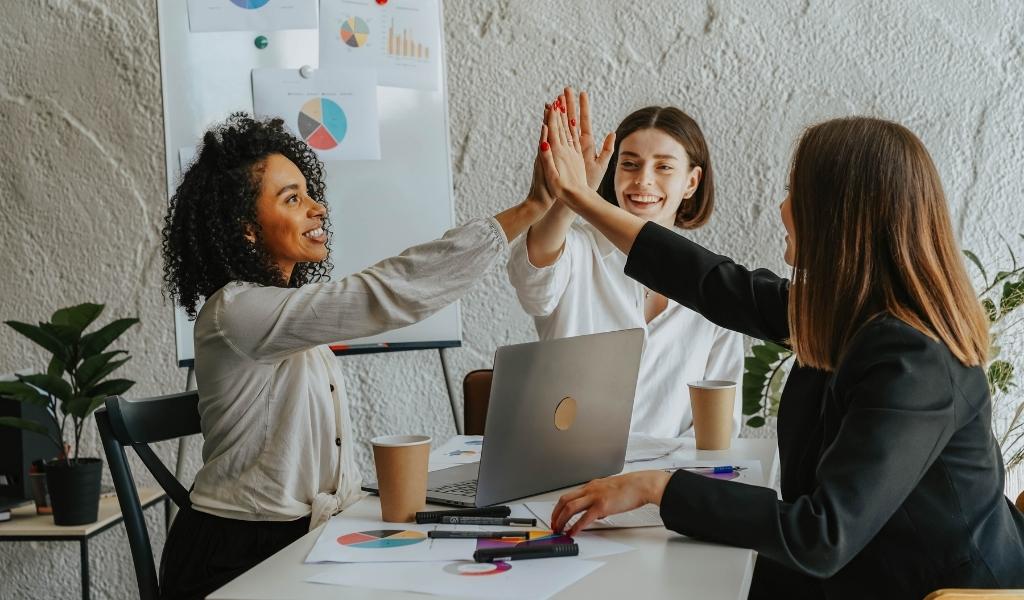 A team of 3 women working together on a project and high-fiving