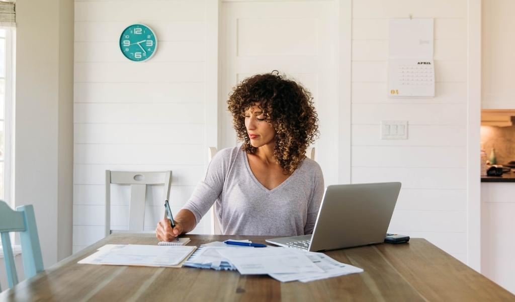 Woman working from home with her laptop open while taking notes