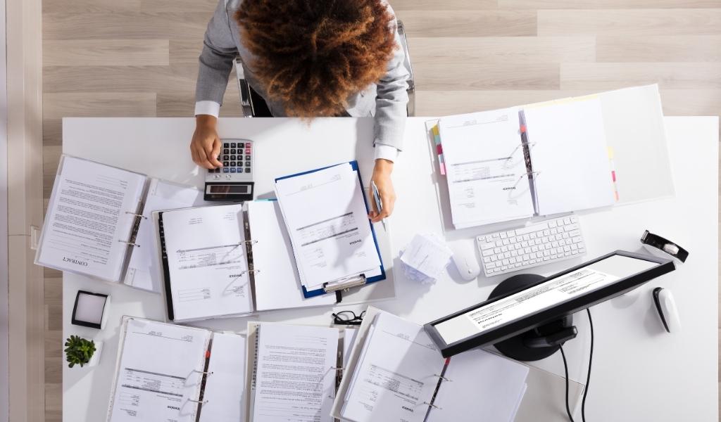 Woman working at a desk filled with different papers and a computer