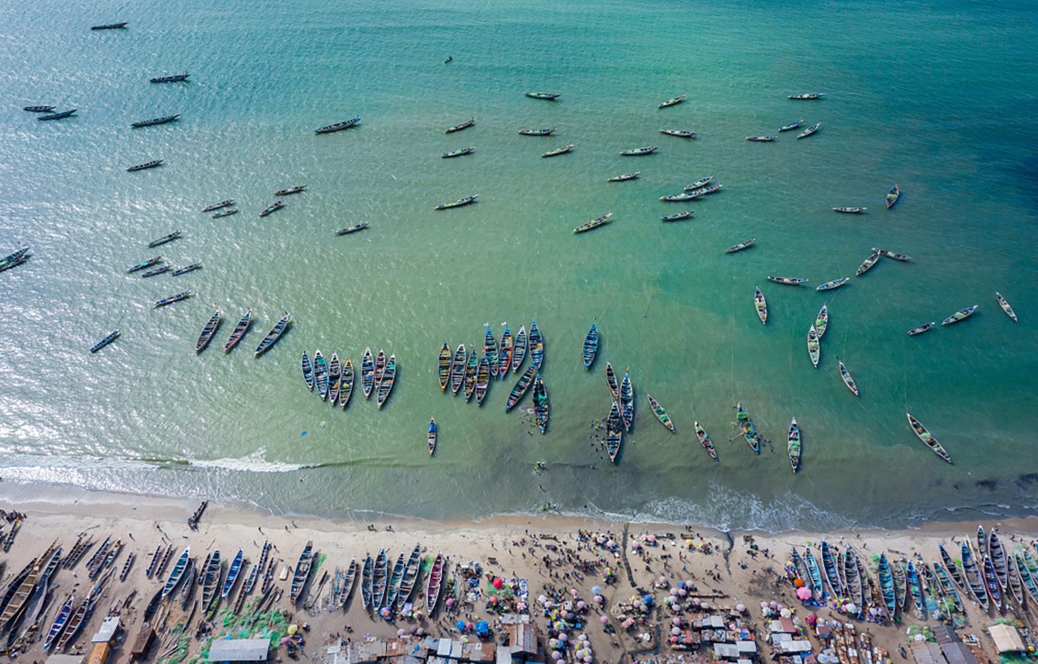 An aerial photo of artisanal fishing boats lined up on the coast of Tanji, a Gambian fishing village
