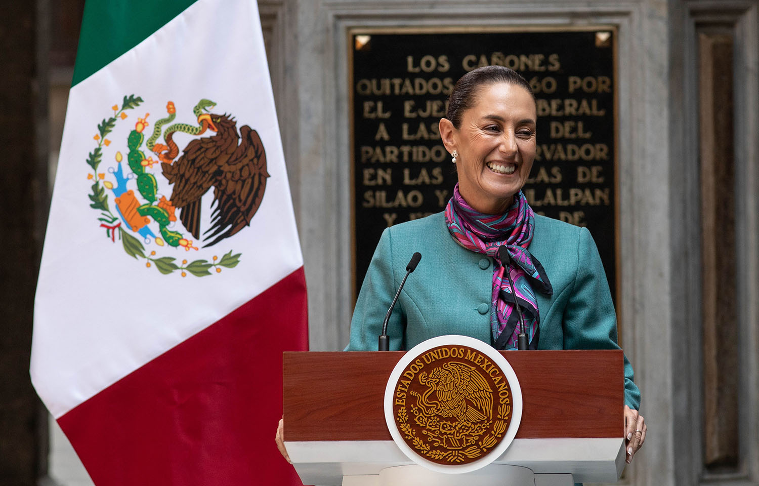 Mexican President Claudia Sheinbaum at a podium in front of the Mexican flag