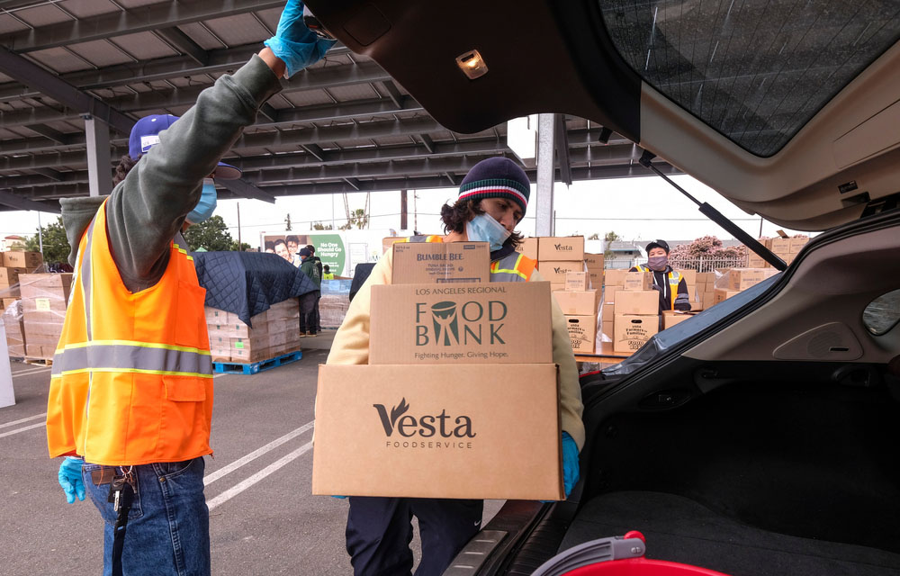 A person at a food bank placing food in the trunk of a car