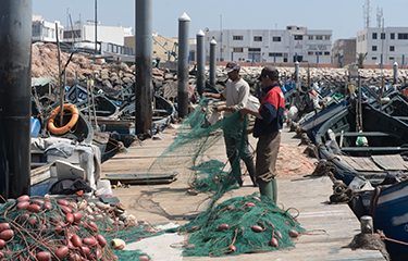 A pair of fishermen maintain nets on a pier in Morocco.