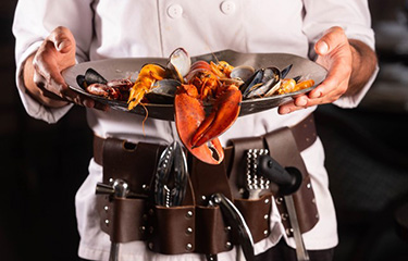 A chef holding a seafood plate with lobster and mussels.