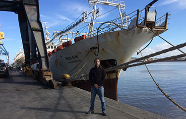 Milko Schvartzman standing on a dock near a fishing vessel.