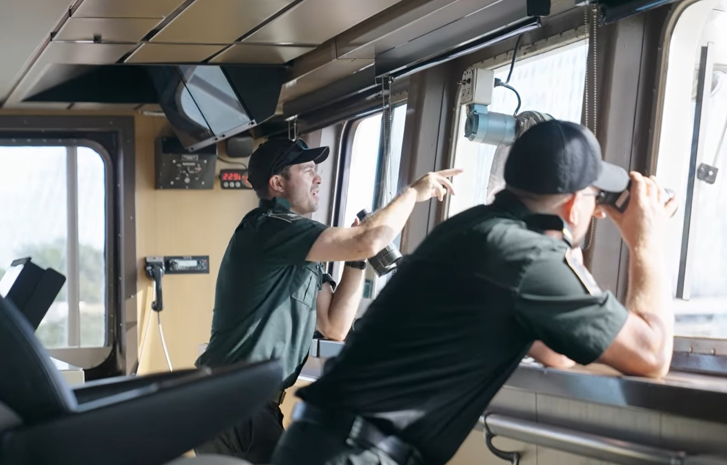 Two Canadian Coast Guard officers on the bridge of the Sir Wilfrid Laurier looking out the windows with binoculars