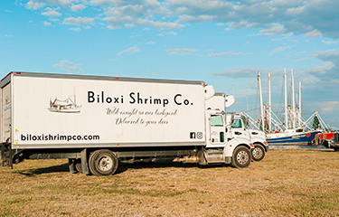 Biloxi Shrimp Co. box trucks parked near Gulf of Mexico shrimp boats.