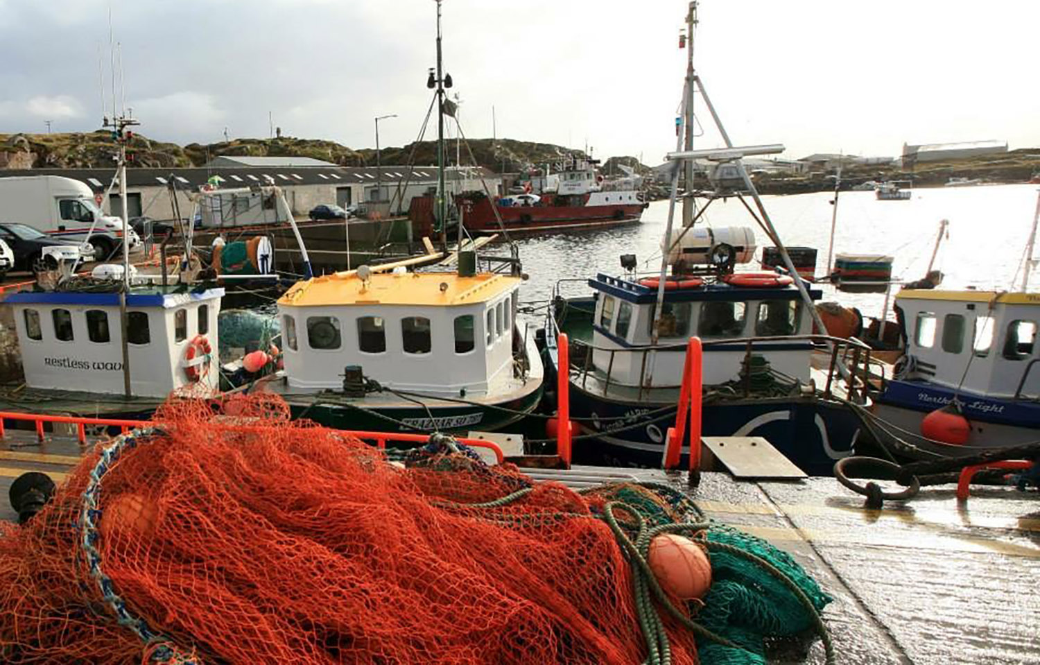 Irish inshore fishing boats lined up at a dock with netting piled up in the foreground