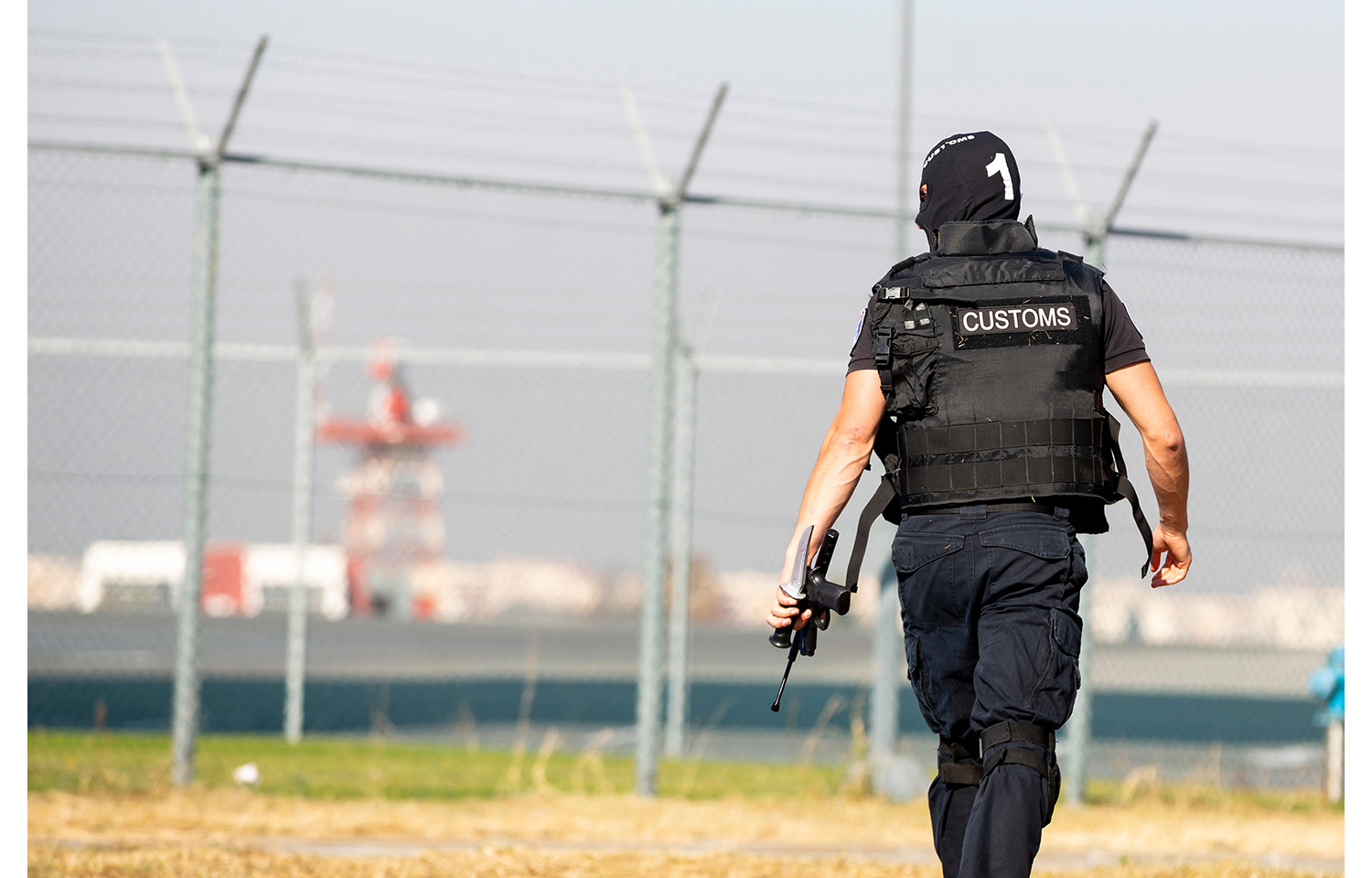 An ICE officer in front of a fence