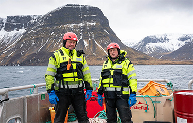 Two workers with Arctic Fish standing by the ocean.