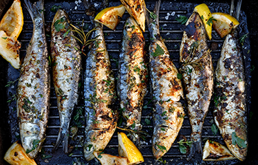 Sardines on a grill with lemon slices.