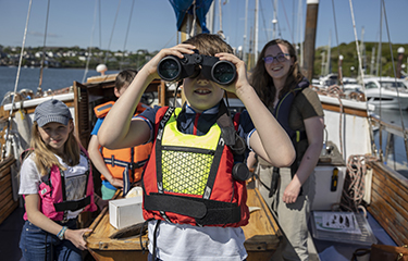 A child looking through binoculars on a sailboat.