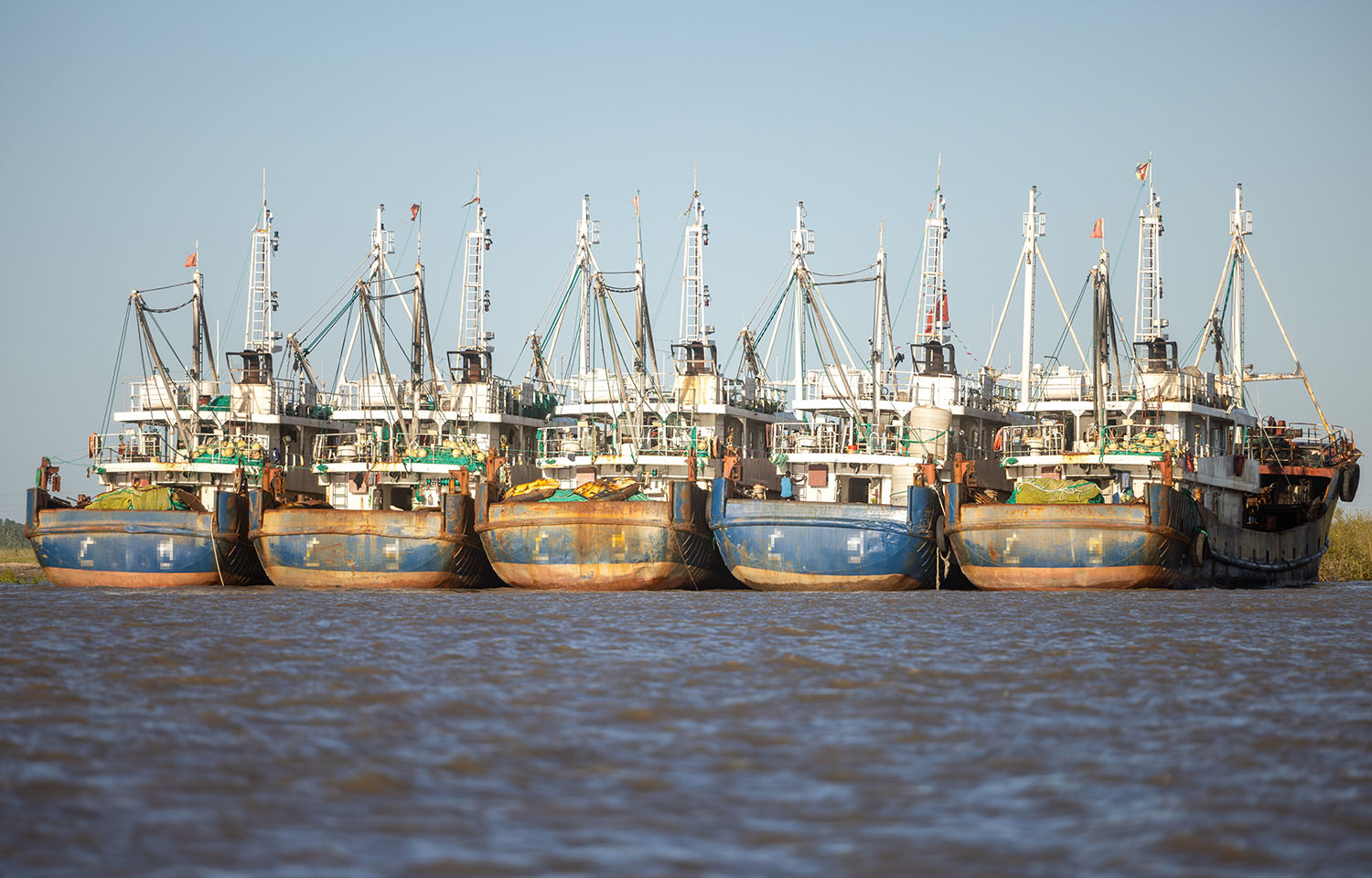 A fleet of Chinese distant water fishing vessel on the water by the shoreline.