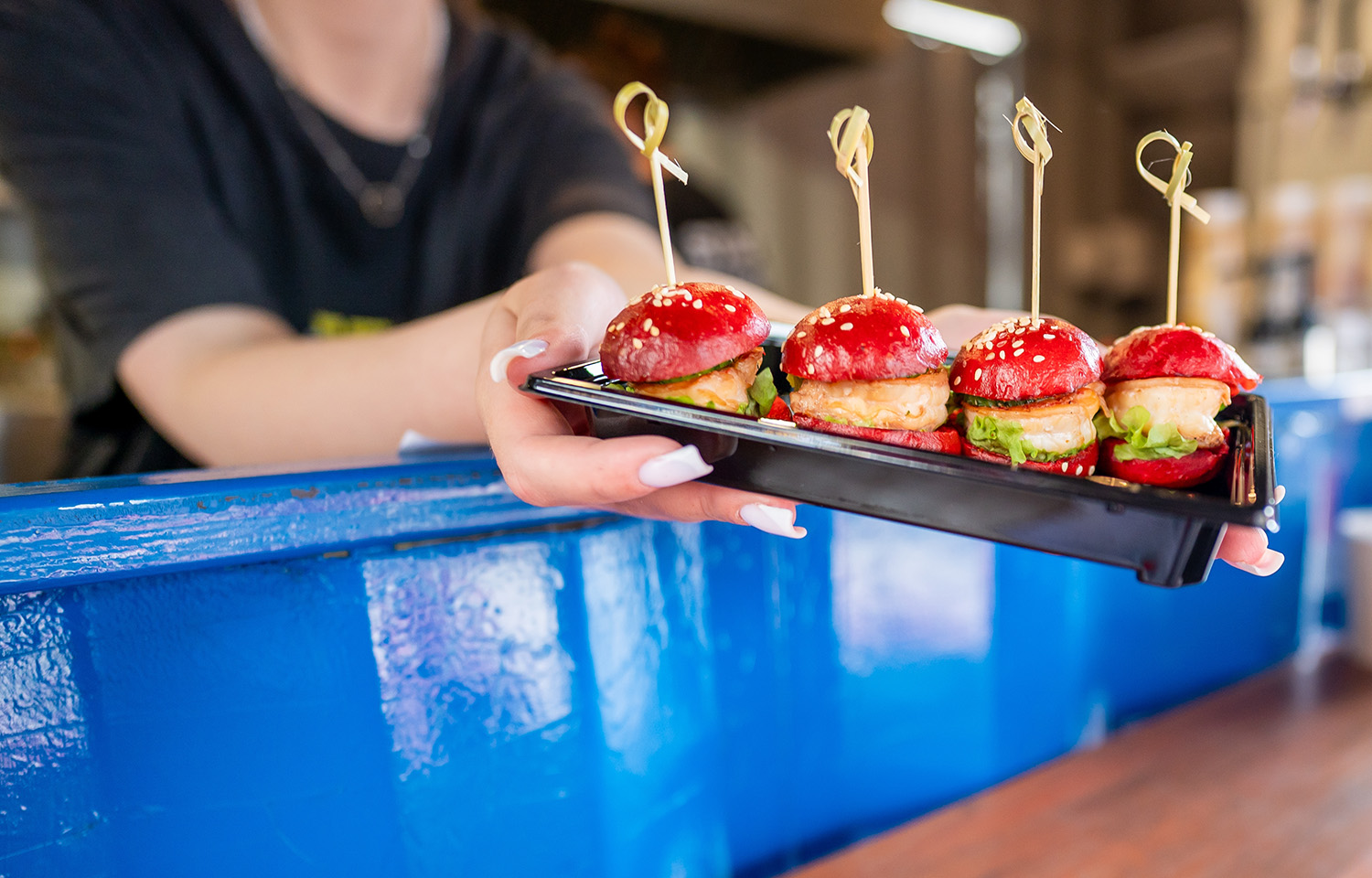 A woman holding out mini shrimp burgers on a tray