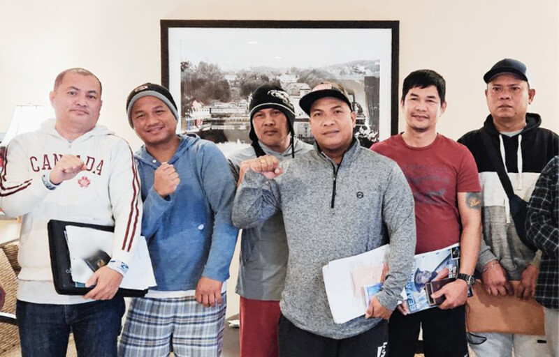 A group of six Filipino men in sweaters holding up their fists