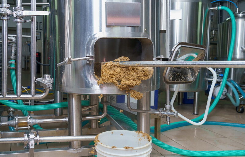 Brewer's spent grain being shoveled out of a stainless steel vat