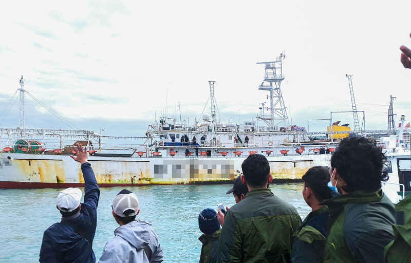 Men on shore wave at a fishing vessel