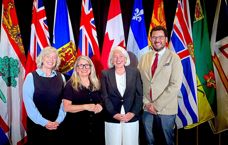Canadian officials standing in front of the country's national and provincial flags