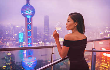 A woman drinking wine at an overlook of Shanghai's skyline.